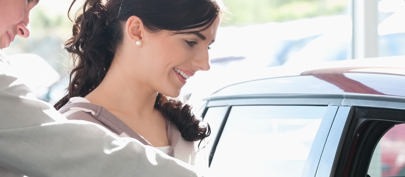 Car dealer pointing the interior of a car with a woman in a car shop