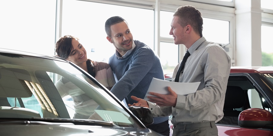 Salesman and a couple looking at a car in a car shop