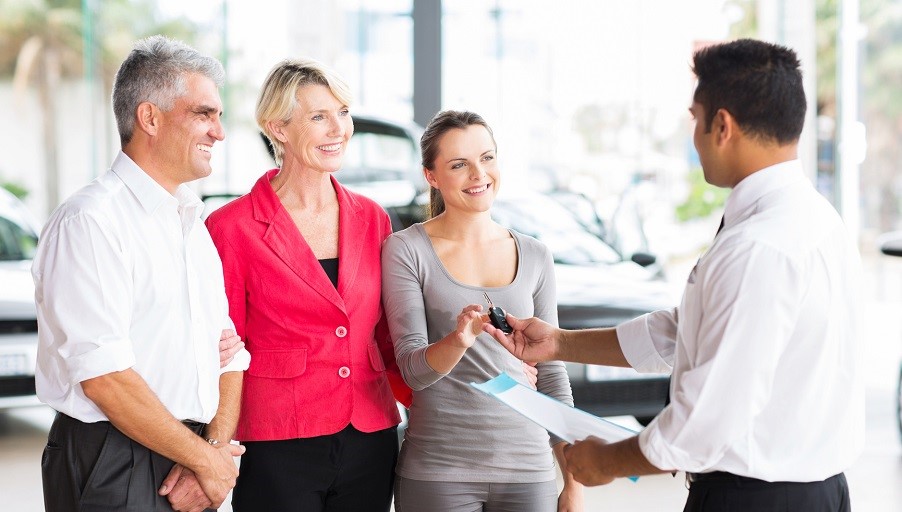 friendly salesman handing car key to customer in showroom