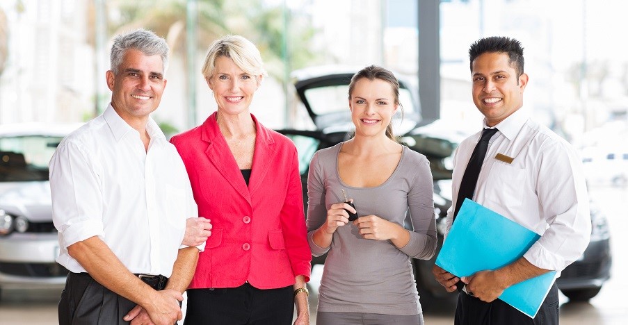 family of three standing with salesman at vehicle dealership after buying a new car