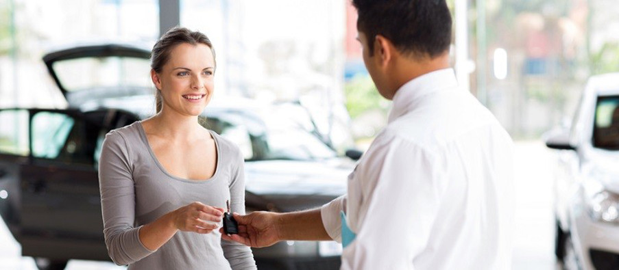 young woman receiving her new car key from salesman