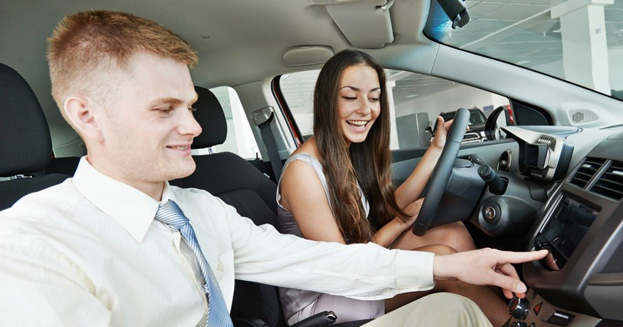 Car salesperson demonstrating new automobile to young woman